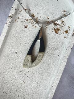 Collier en porcelaine noire avec effet Light Magma posé à plat – bijou fait main par Honey Dew. Détails uniques visibles sur la texture. Parfait pour les amatrices de pièces sobres et singulières. / Belgische porselein ketting – elk stuk is uniek / Unique handmade necklace – Light Magma finish by Honey Dew, Belgium