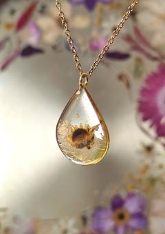 Pendentif goutte lumineuse avec fleur dorée encapsulée, bijou artisanal Noémie de B&L Atelier livré en écrin cadeau / Lichtgevende druppelhanger met ingesloten gouden bloem, handgemaakt door Noémie – B&L Atelier en geleverd in geschenkdoos / Luminous drop pendant with encapsulated golden flower by Noémie – B&L Atelier, delivered in a gift box