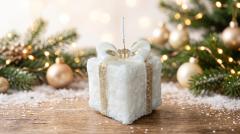 Bougie de Noël bio parfumée en forme de paquet cadeau blanc près d'un sapin – Lueur de Flo / Biologische geurkaars in de vorm van een wit kerstcadeautje bij de kerstboom – Lueur de Flo / Organic scented candle shaped like a white Christmas gift by the tree – Lueur de Flo